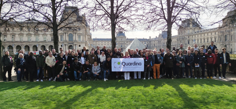 Groupe devant la pyramide du Louvre à Paris avec bannièere du logo Quardina